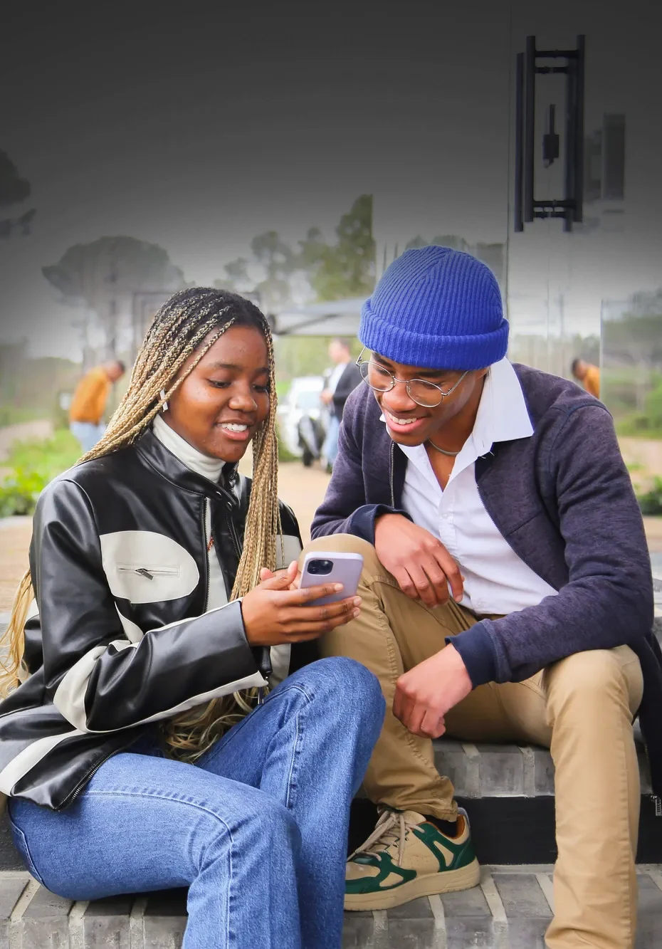 Two students sit on stairs, looking at a phone screen together.